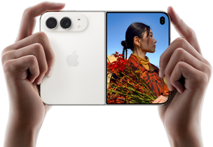 جهاز iPhone Duo، لون أبيض النجوم، يدان تحملان الجهاز في الوضع الأفقي، مفتوح، اللوحة اليسرى تعرض نظام كاميرا مزدوجة 48MP Fusion، اللوحة اليمنى تعرض شخصاً تُلتقط صورته على الشاشة الخارجية، يمكن لهذا الشخص رؤية وجهه لأن الصورة تُلتقط باستخدام ميزة Duo Preview